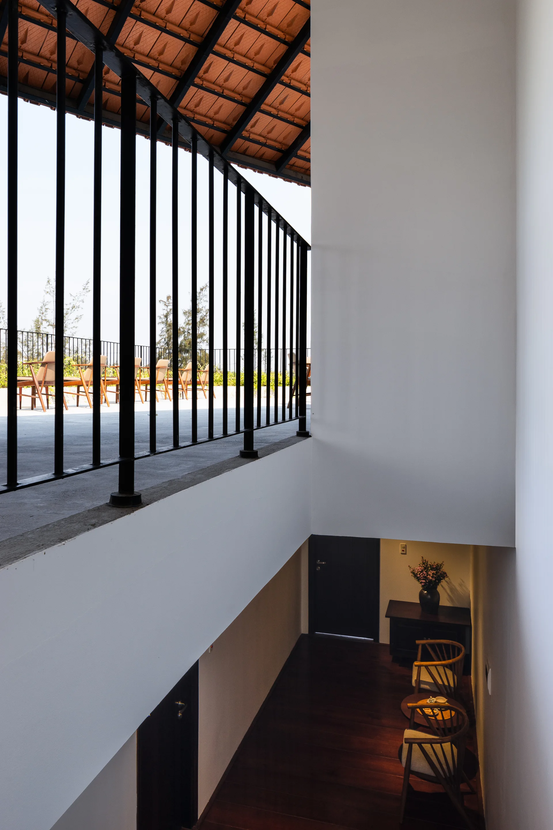 A split-level interior landing features white walls, a black metal balcony railing, and a lower level with dark wood floors and armchairs.