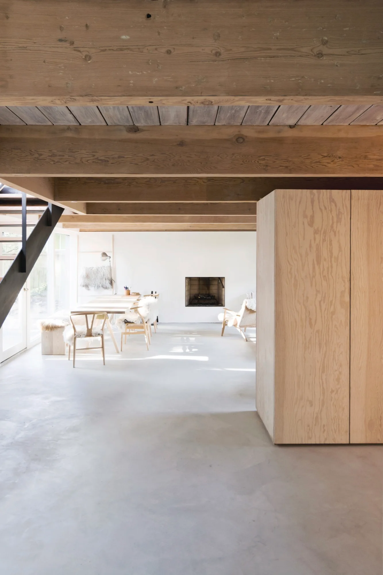 An open living room features heavy wood ceiling beams, smooth concrete floors, a recessed fireplace, and a light wood dining set.
