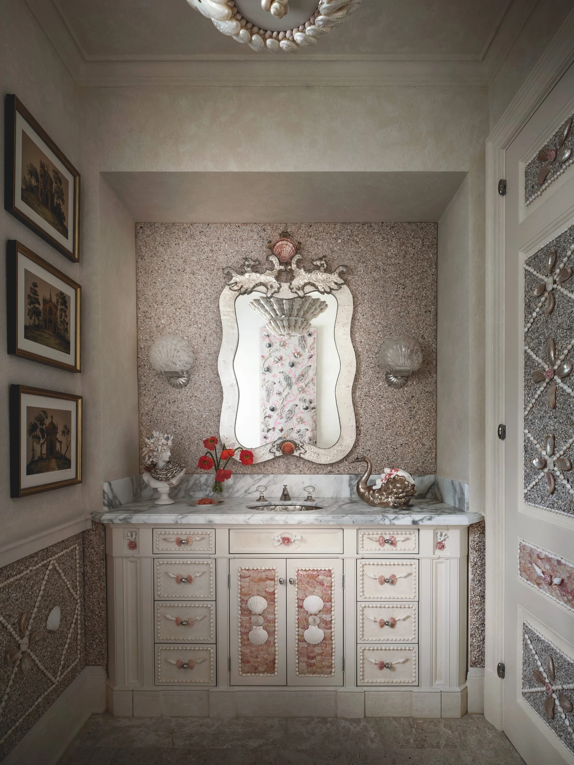 A powder room features a custom cream vanity decorated with intricate seashell patterns, a marble countertop, and an ornate matching mirror.