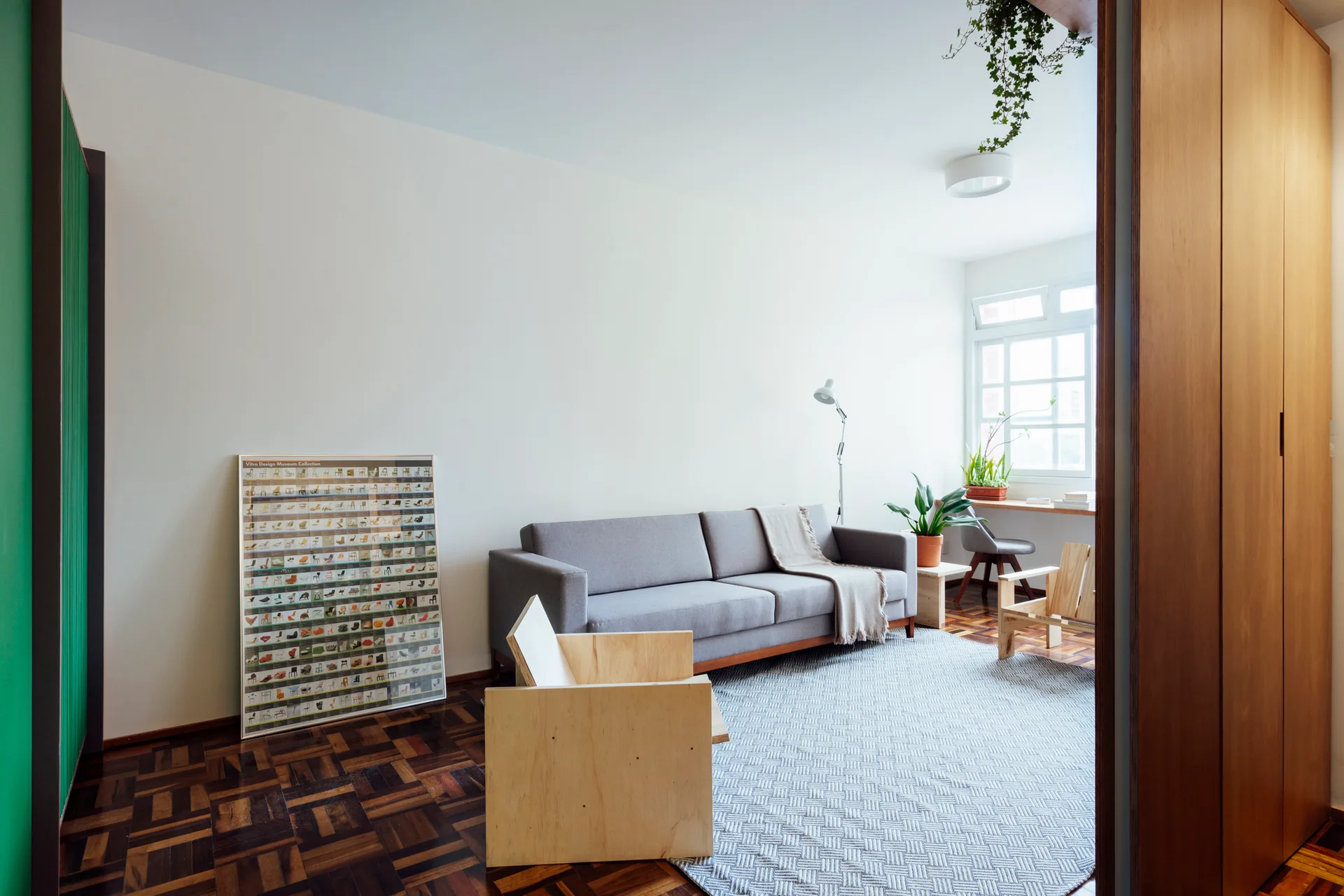 A minimalist living room features a grey sofa, a geometric pattern rug over parquet wood flooring, and a boxy light wood armchair in the foreground.