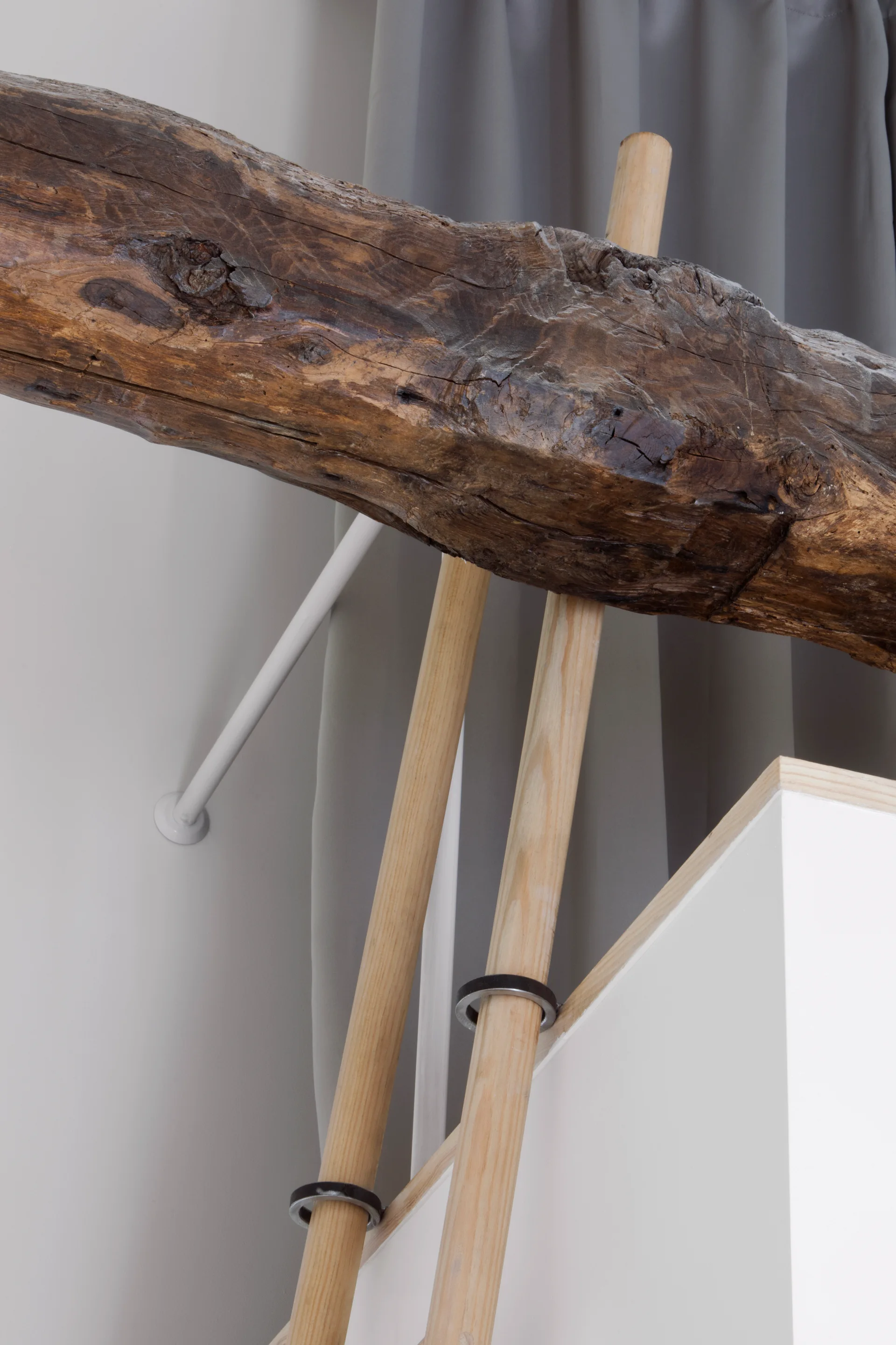 A close-up of a weathered, dark brown wooden ceiling beam positioned above a light wood ladder and grey curtains.