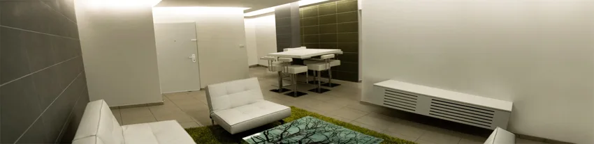 A minimalist living space featuring white tufted sofas, a bright green rug, a graphic coffee table, and a wall-mounted slatted console cabinet.