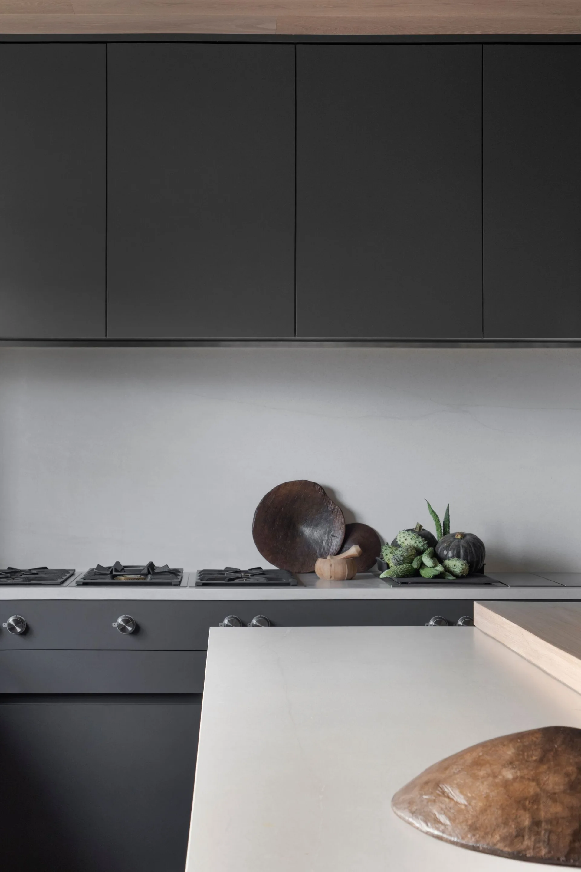 A modern minimalist kitchen featuring dark matte charcoal upper cabinetry, a gas stovetop, and a light grey stone countertop and backsplash.