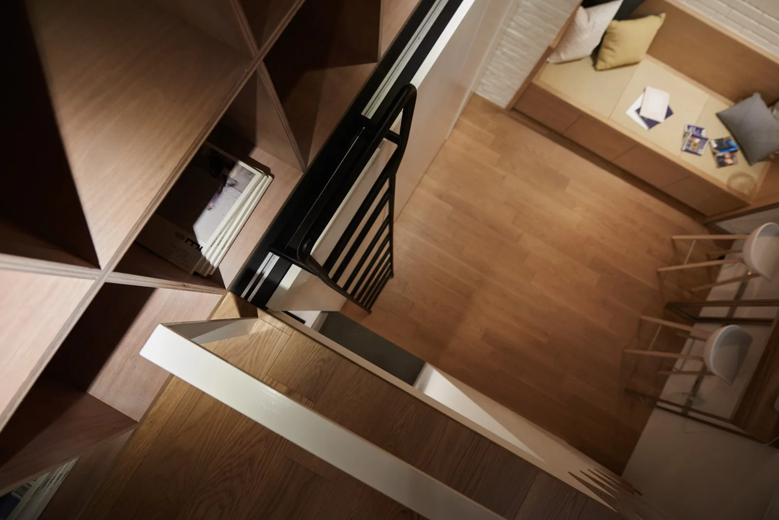 A high-angle view looking down at a wooden shelving unit with a black rolling ladder, wood floors, and a built-in bench below.