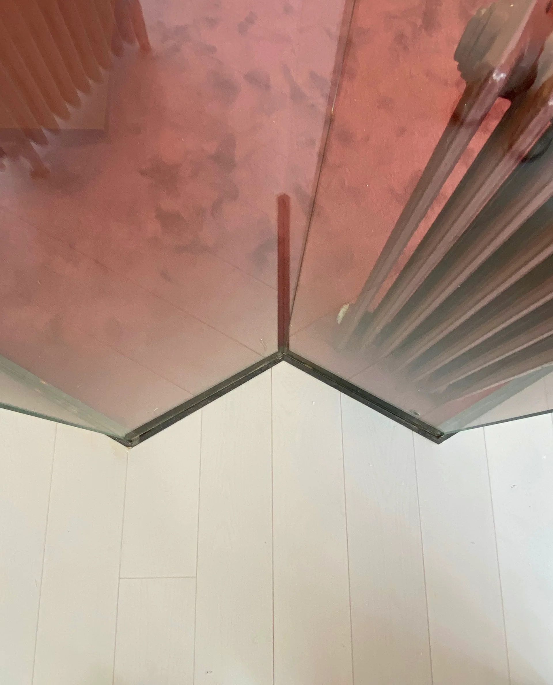 A close-up view of an angled pink translucent glass room divider resting on a light-colored wood plank floor.