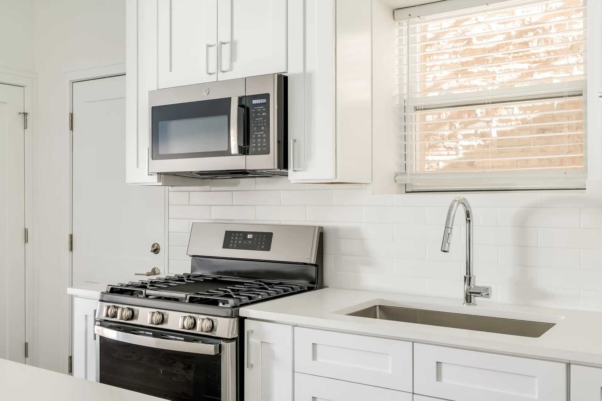 A bright white kitchen showcases shaker-style cabinets, a matching subway tile backsplash, a stainless steel gas range, and an undermount sink.