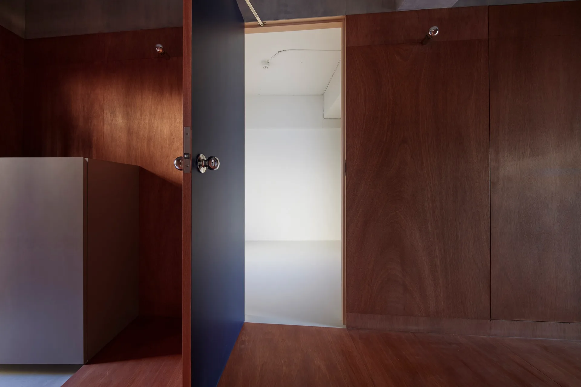 An open navy blue door with a round metal doorknob stands within a dark wood-paneled room, leading into a bright white space.