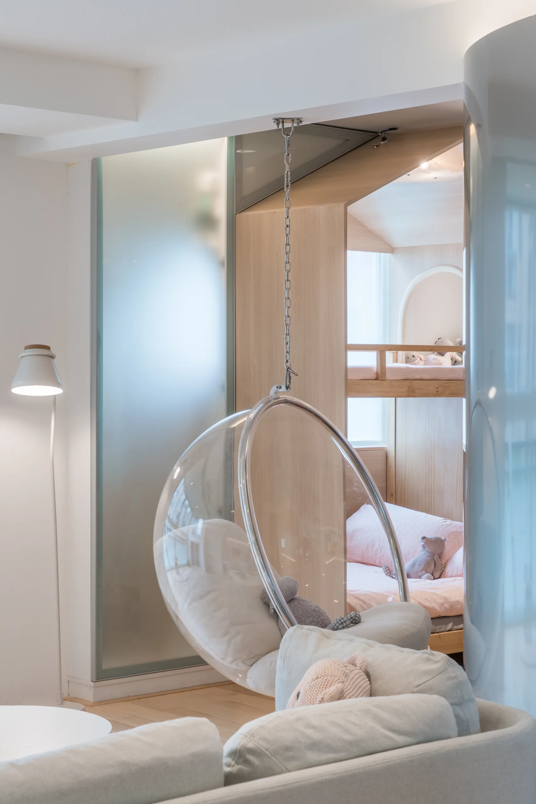 A children's bedroom features a transparent hanging bubble chair in front of a light wood bunk bed nook and a frosted glass sliding door.