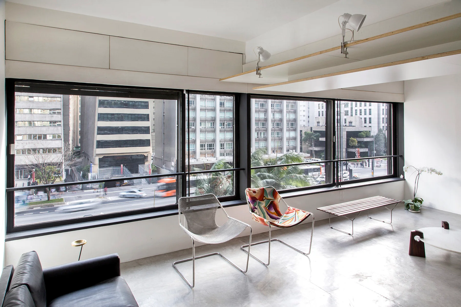 A minimalist living room features a polished concrete floor, modern chairs, and large windows overlooking a busy city street.