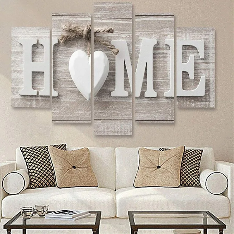 A white upholstered sofa with checkered and beige pillows sits below a five-piece canvas wall art display reading HOME.
