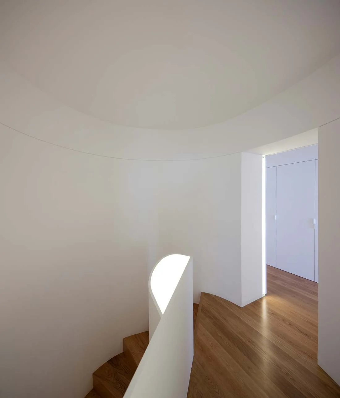 A curved white staircase features wood treads, smooth plaster-style walls, and an integrated glowing light strip along the interior banister.