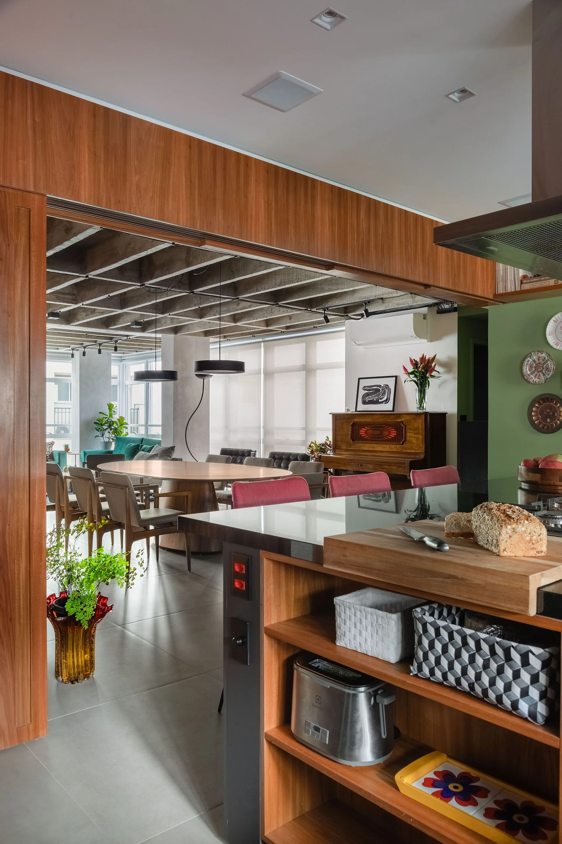 A wooden kitchen island in the foreground looks out toward a round dining table set under an exposed concrete waffle ceiling.