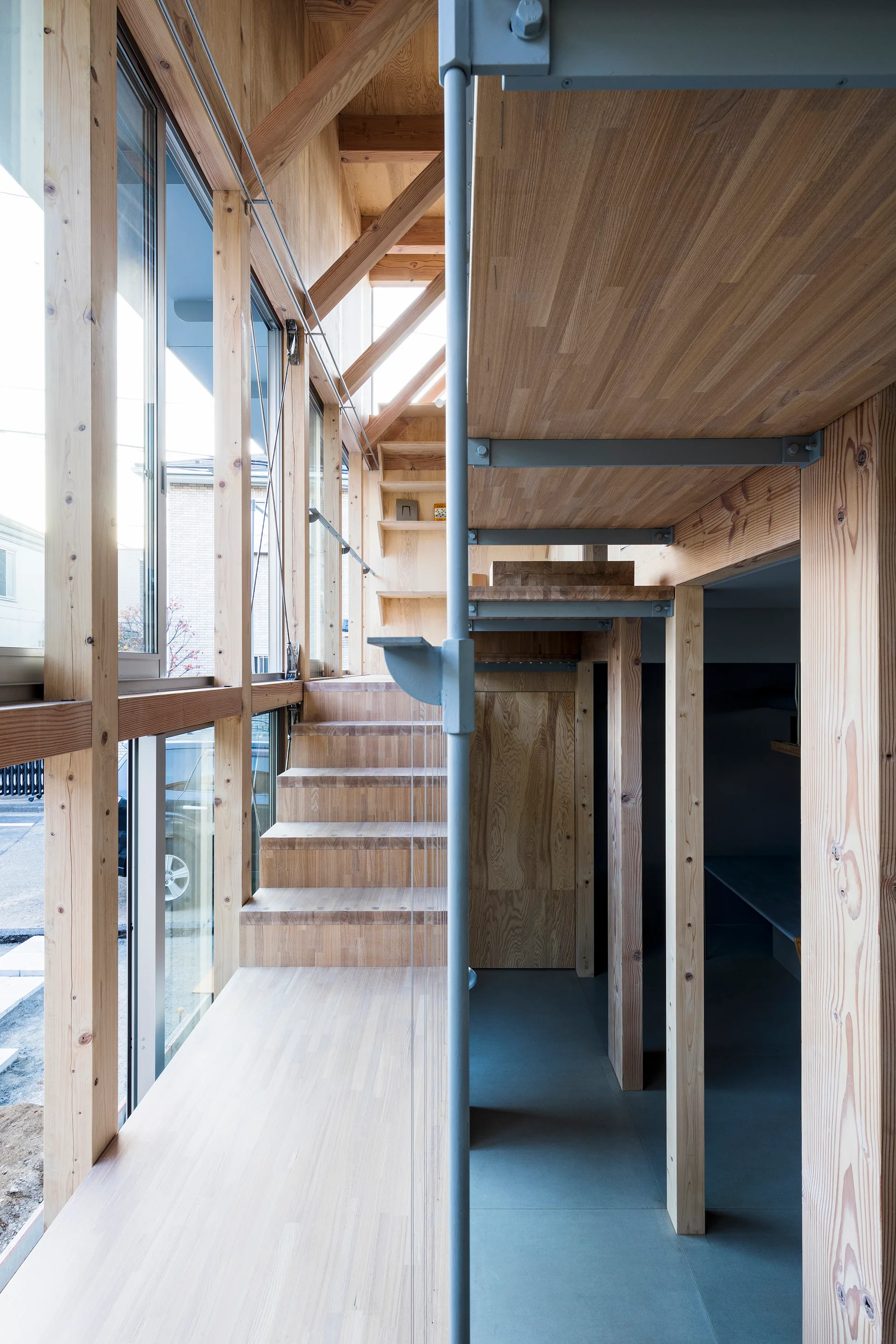 A modern residential interior featuring a wooden staircase, exposed timber framing, large glass windows, and a matte grey floor.