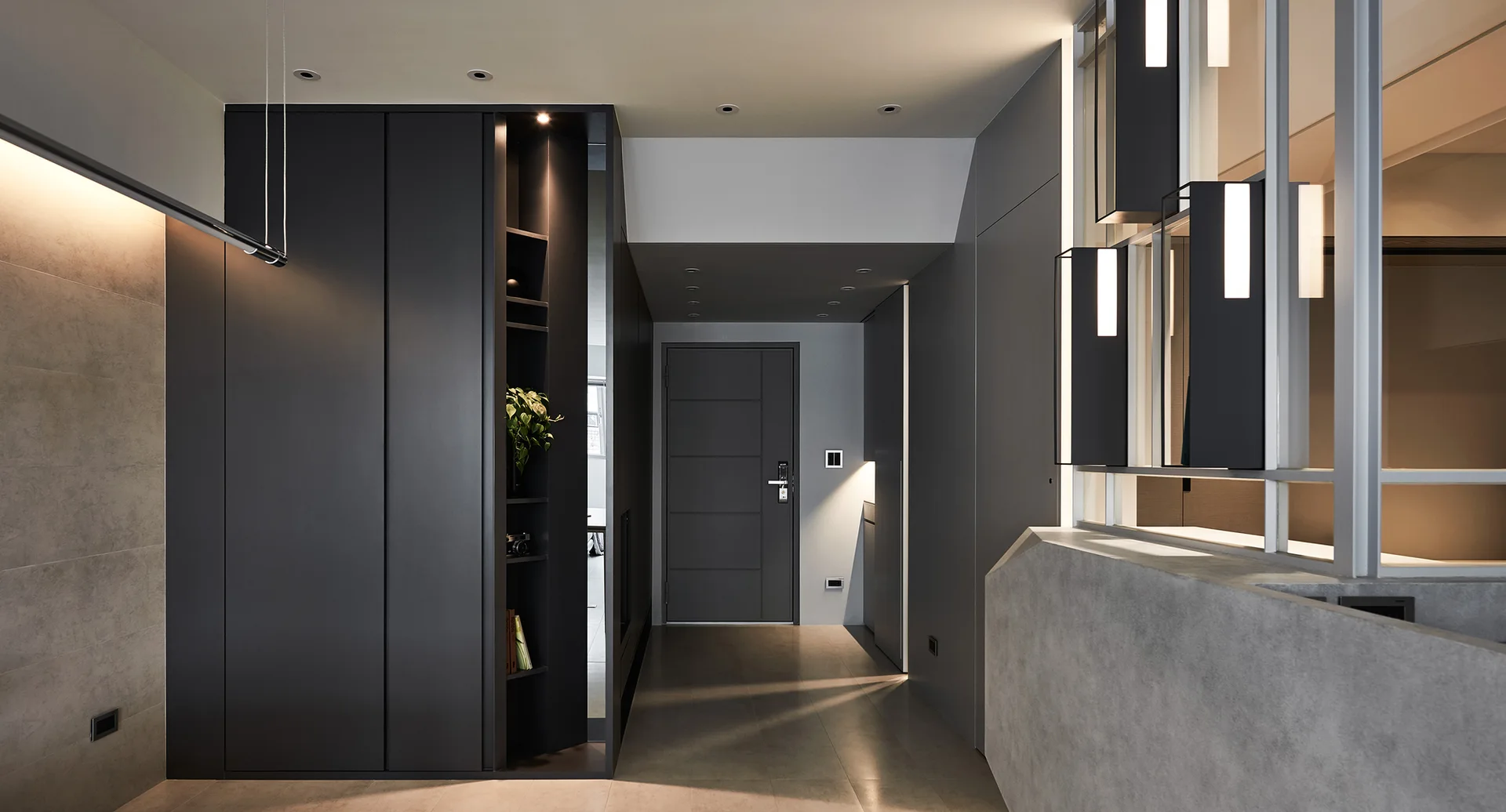 A minimalist modern entryway features matte charcoal grey built-in cabinetry with a lit display niche, large-format floor tiles, and a glass partition.