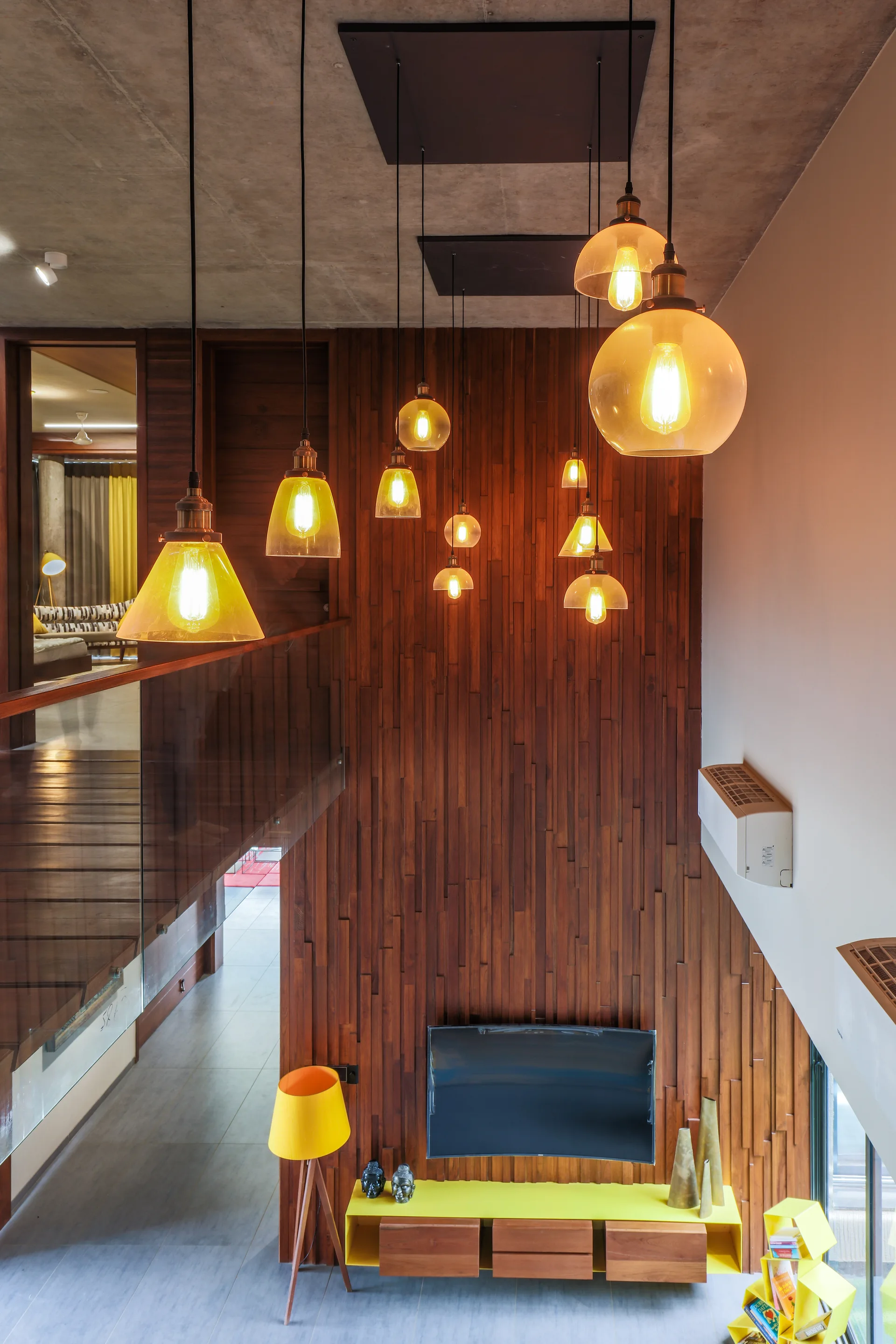 A high-angle view of a living room with a vertical wood slat accent wall, staggered glass pendant lights, and a yellow media console.