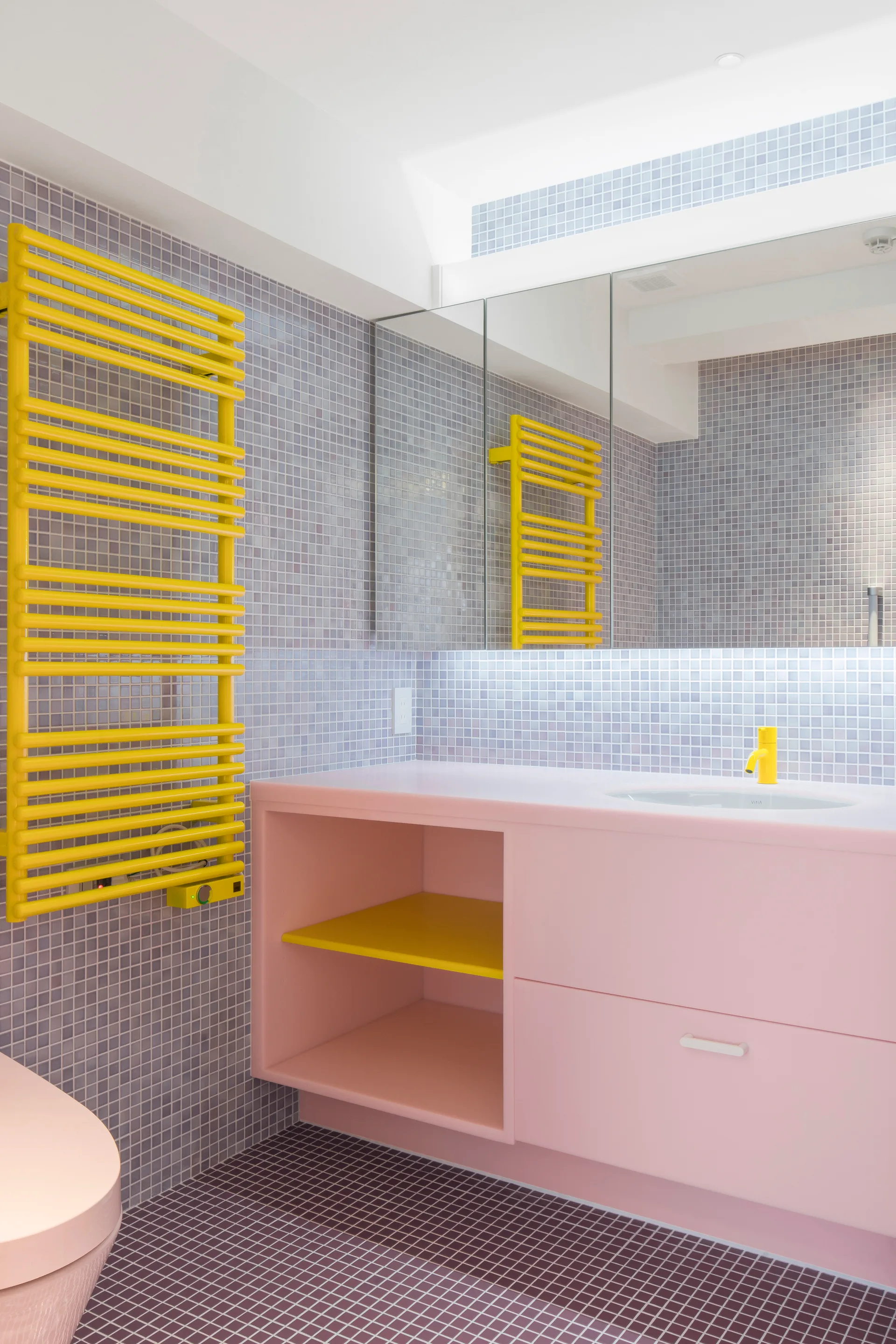 A bathroom features lavender mosaic tile walls, a pink floating vanity with a yellow faucet, and a bright yellow ladder towel warmer.