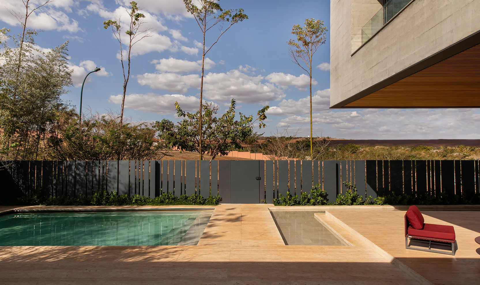 A modern outdoor terrace features a turquoise swimming pool, a stone patio, and a dark grey vertical-slat fence beneath a concrete cantilever roof.