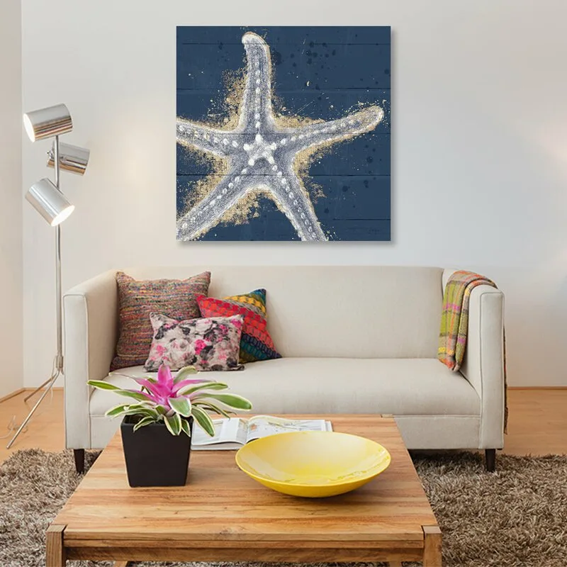 A beige sofa with colorful pillows sits beneath a blue starfish painting, with a wooden coffee table and a metal floor lamp nearby.
