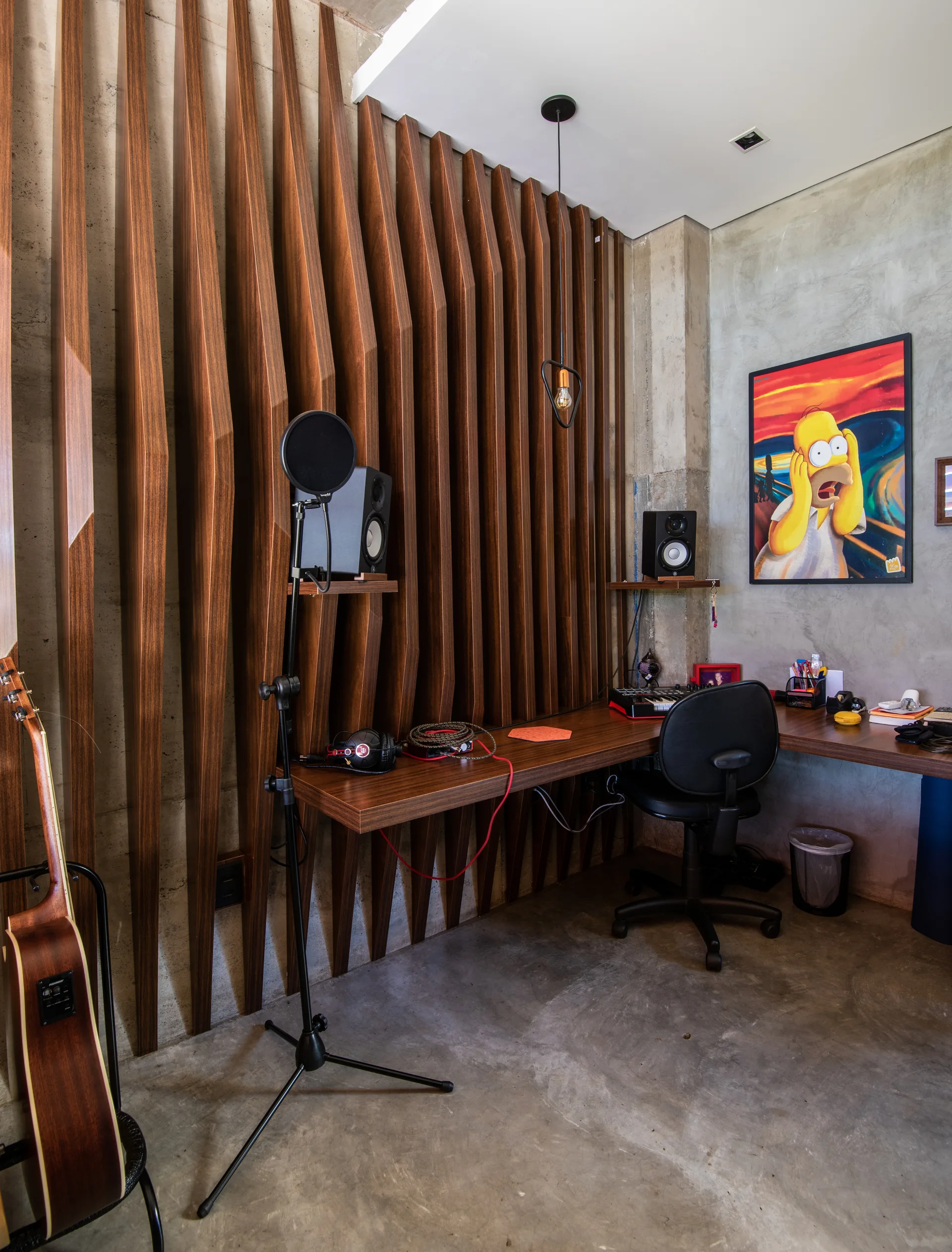 A home recording studio features a floating wooden desk, vertical wood slats on the wall, and exposed concrete surfaces.