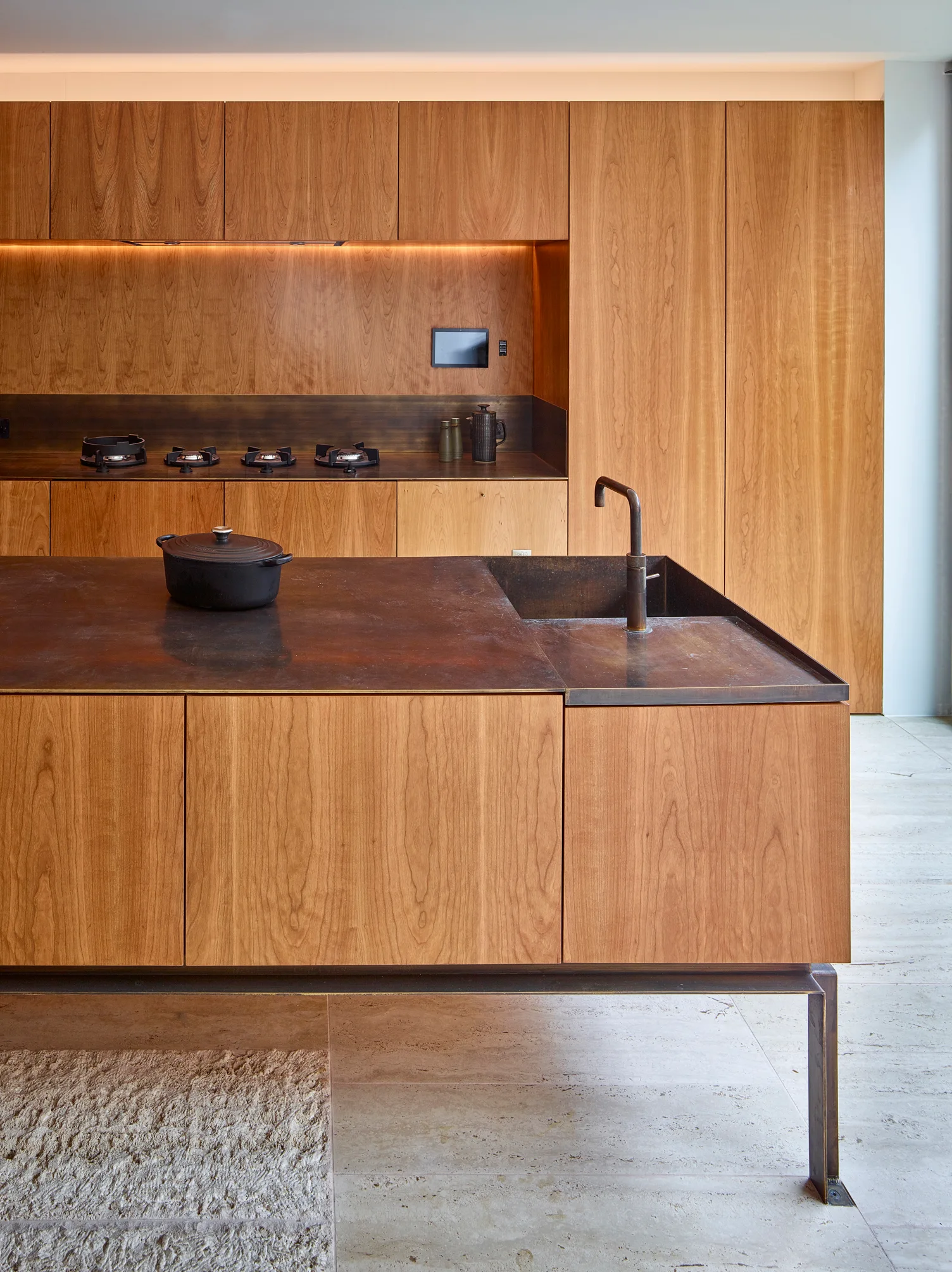 A minimalist modern kitchen featuring warm wood-grain cabinetry, a matching kitchen island on slim metal legs, and a patinated bronze countertop.