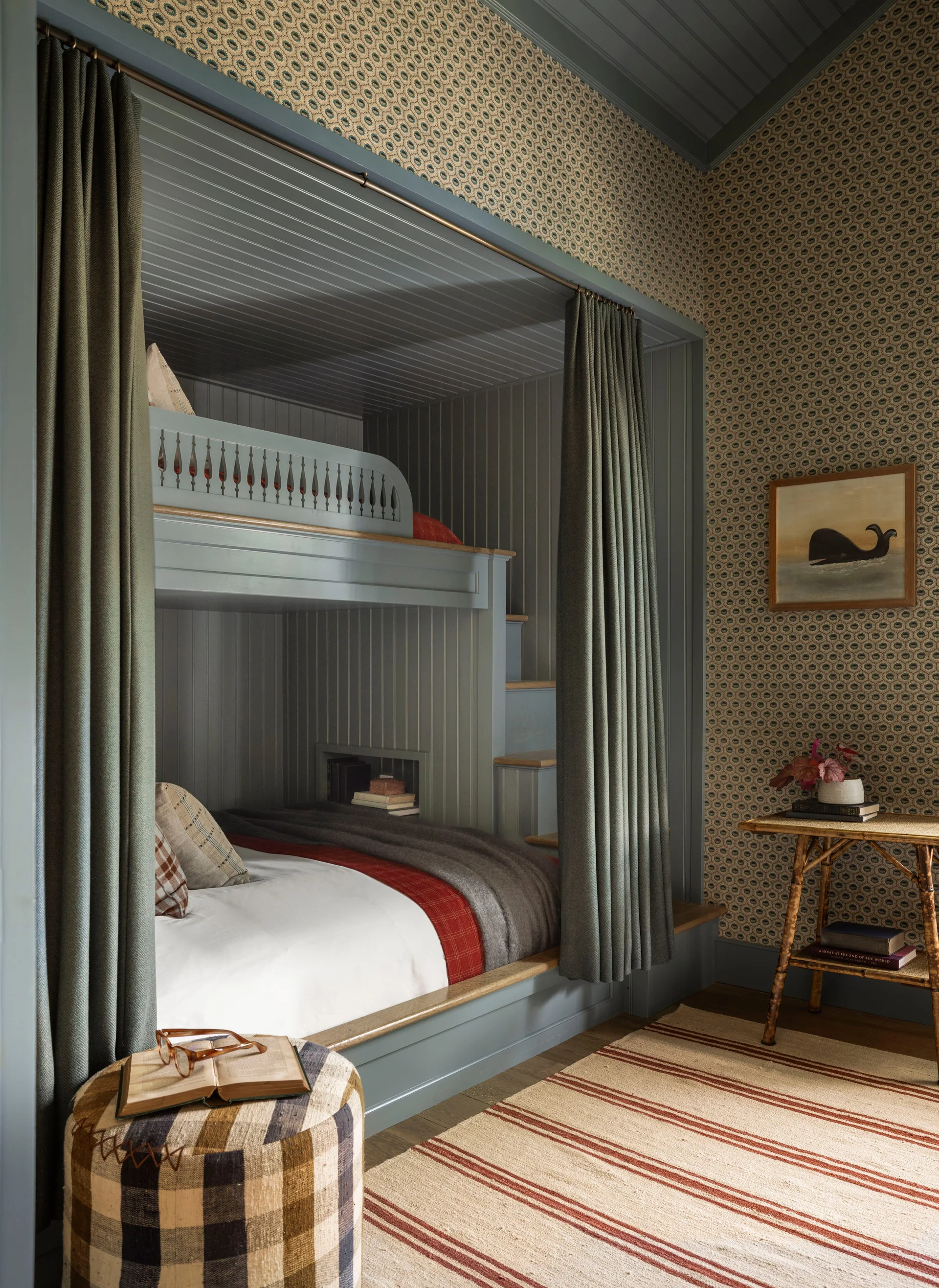 A bedroom features a slate blue built-in bunk bed with integrated steps, olive green privacy curtains, and patterned wallpaper.