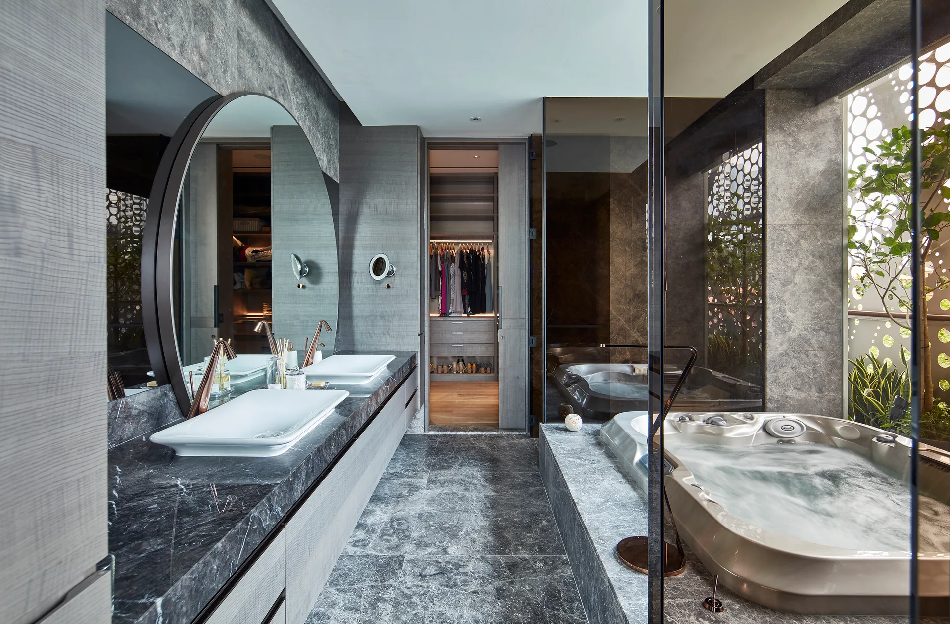 A modern luxury bathroom featuring grey marble walls and floors, a floating double vanity with round mirrors, and a jetted bathtub.