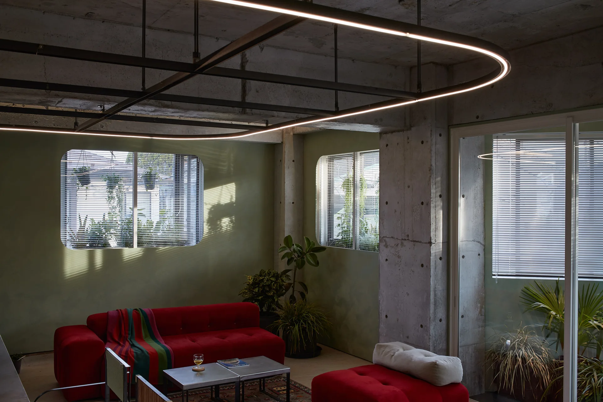 A modern living room featuring a bright red sofa set against olive green walls and an exposed raw concrete ceiling and column.