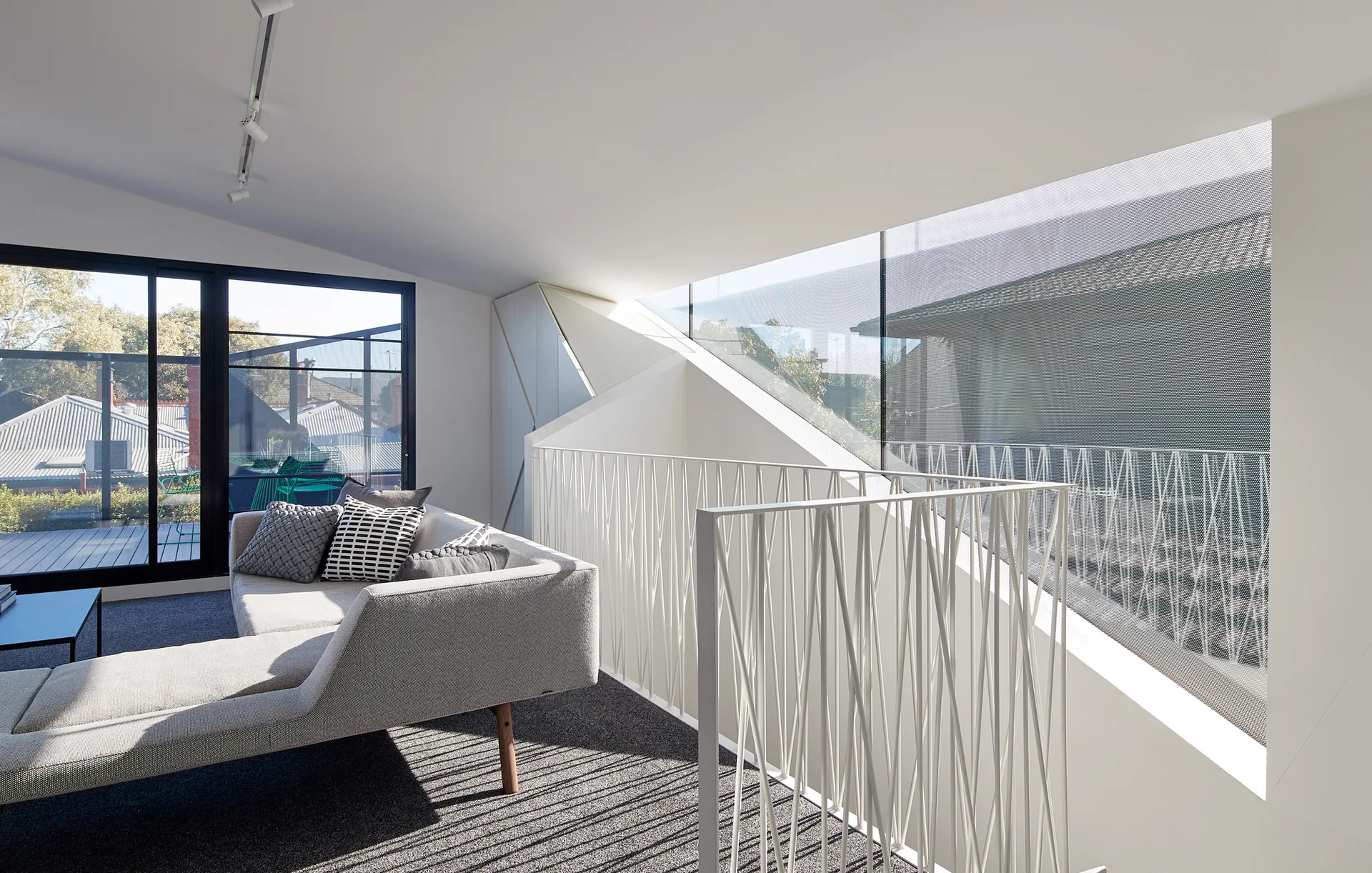 A modern loft living room features a light grey sofa on dark grey carpet beside an abstract white metal railing and a large window.