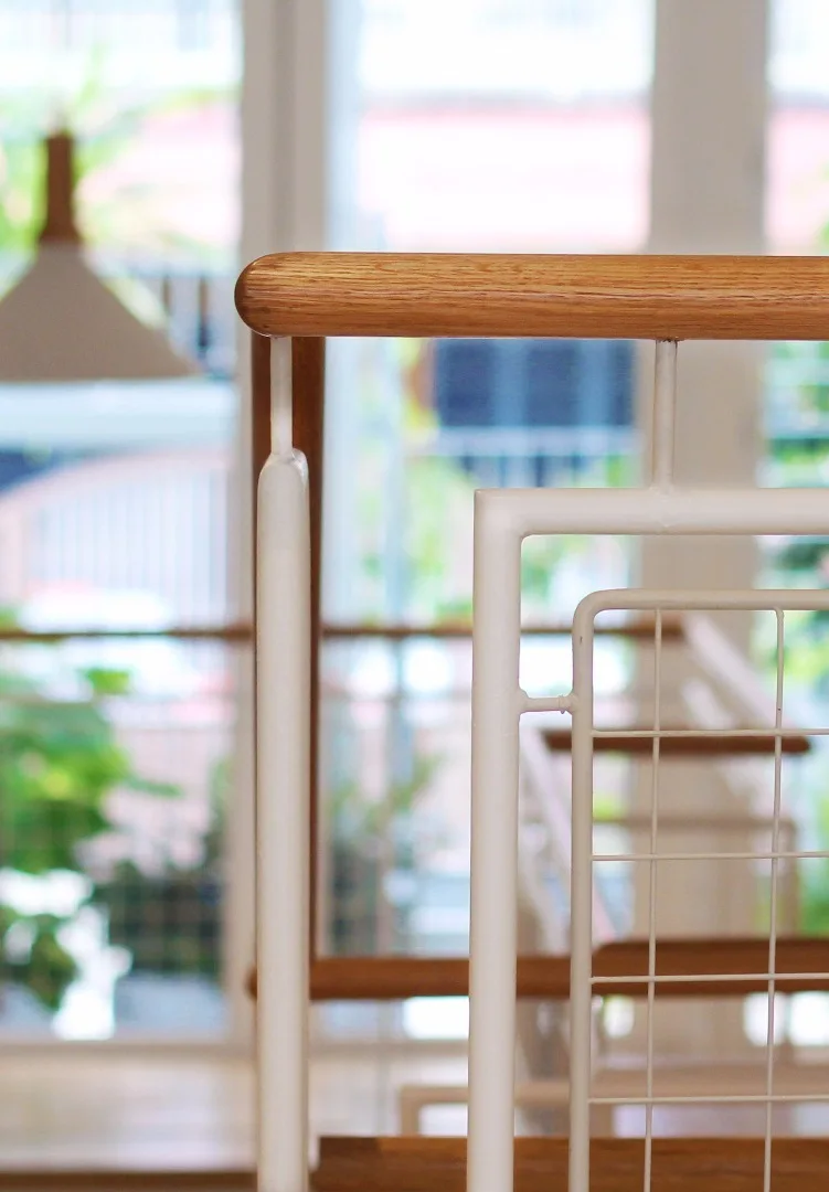 A close-up view of a modern stair railing featuring a natural wood handrail and a white painted metal frame with a grid-patterned panel.