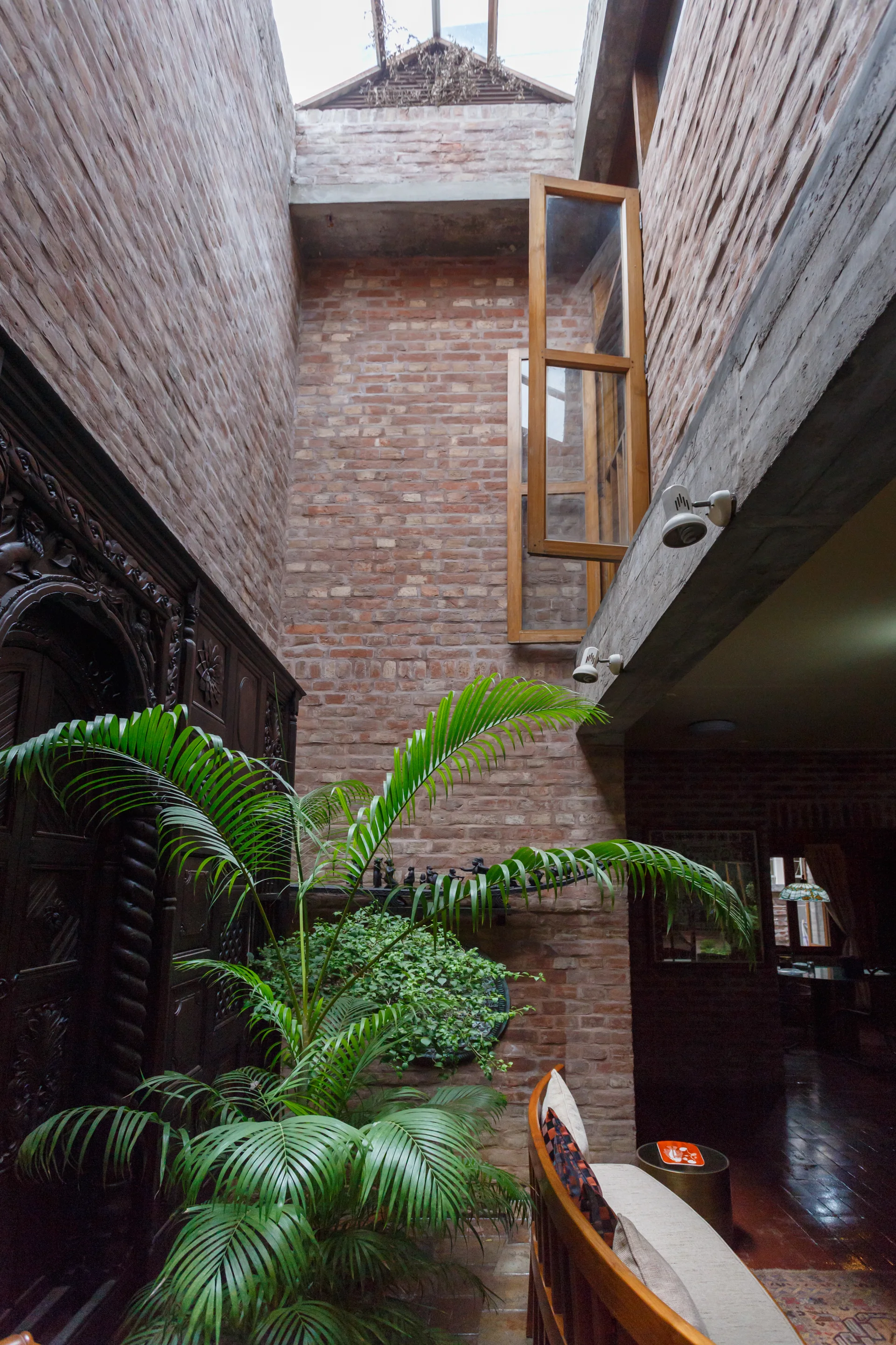 A tall indoor atrium with exposed red brick walls, a skylight overhead, a green potted palm, and an ornate carved wooden door.