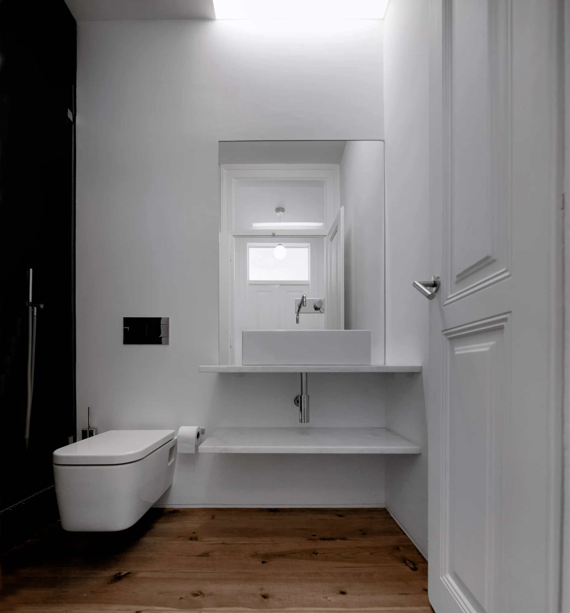 A minimalist white powder room features a wall-mounted toilet, a floating marble-shelf vanity with a vessel sink, and natural wood plank flooring.