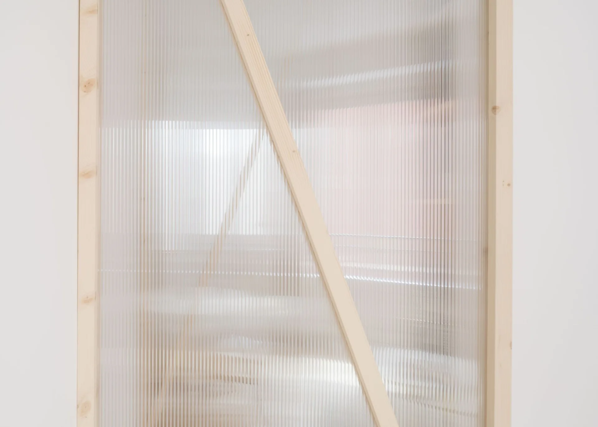 A room partition features a translucent ribbed panel mounted inside an unfinished light wood frame with a diagonal brace.