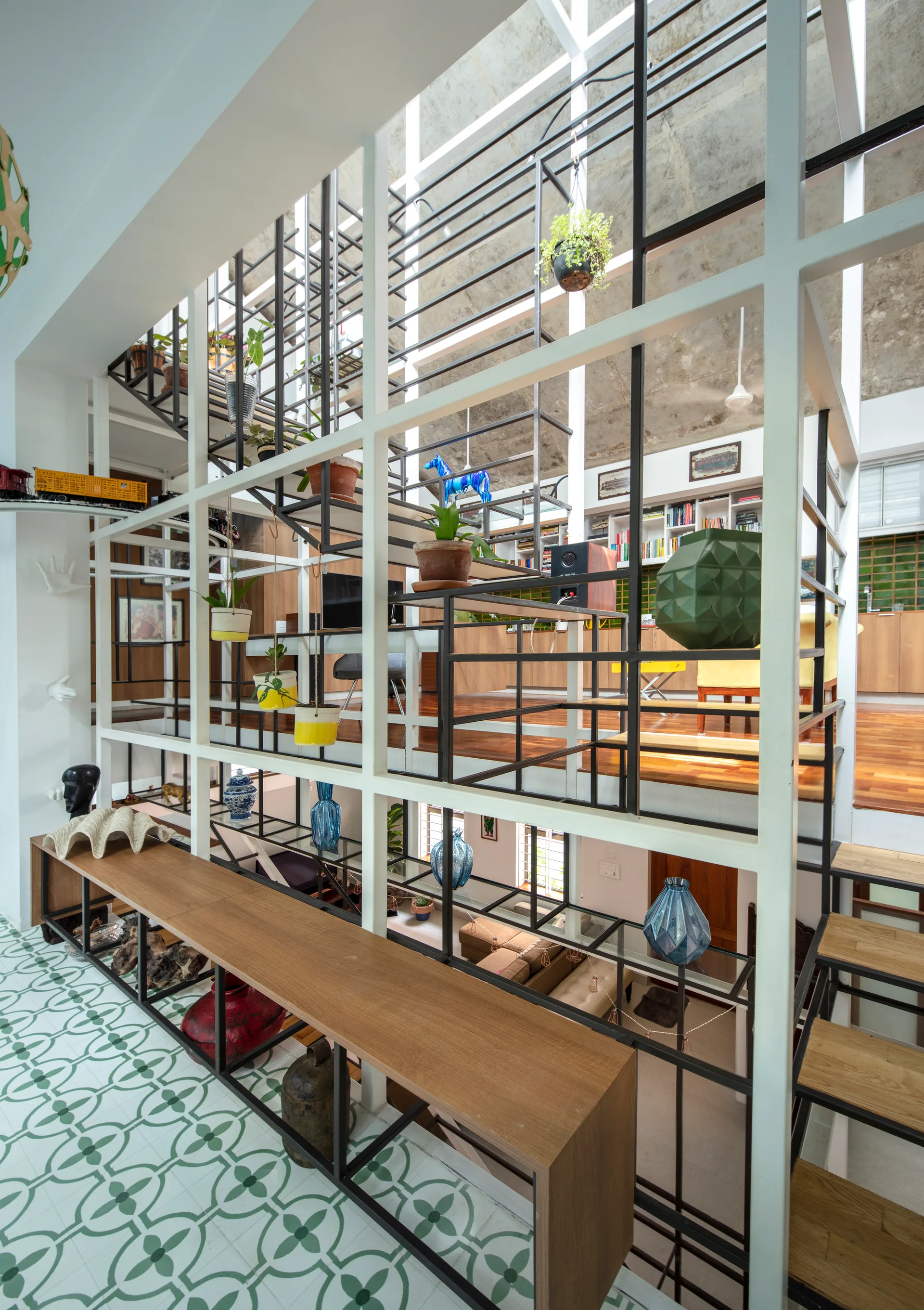 A multi-level home interior features a large white and black metal structural grid partition, green patterned tile flooring, and a long wood console.