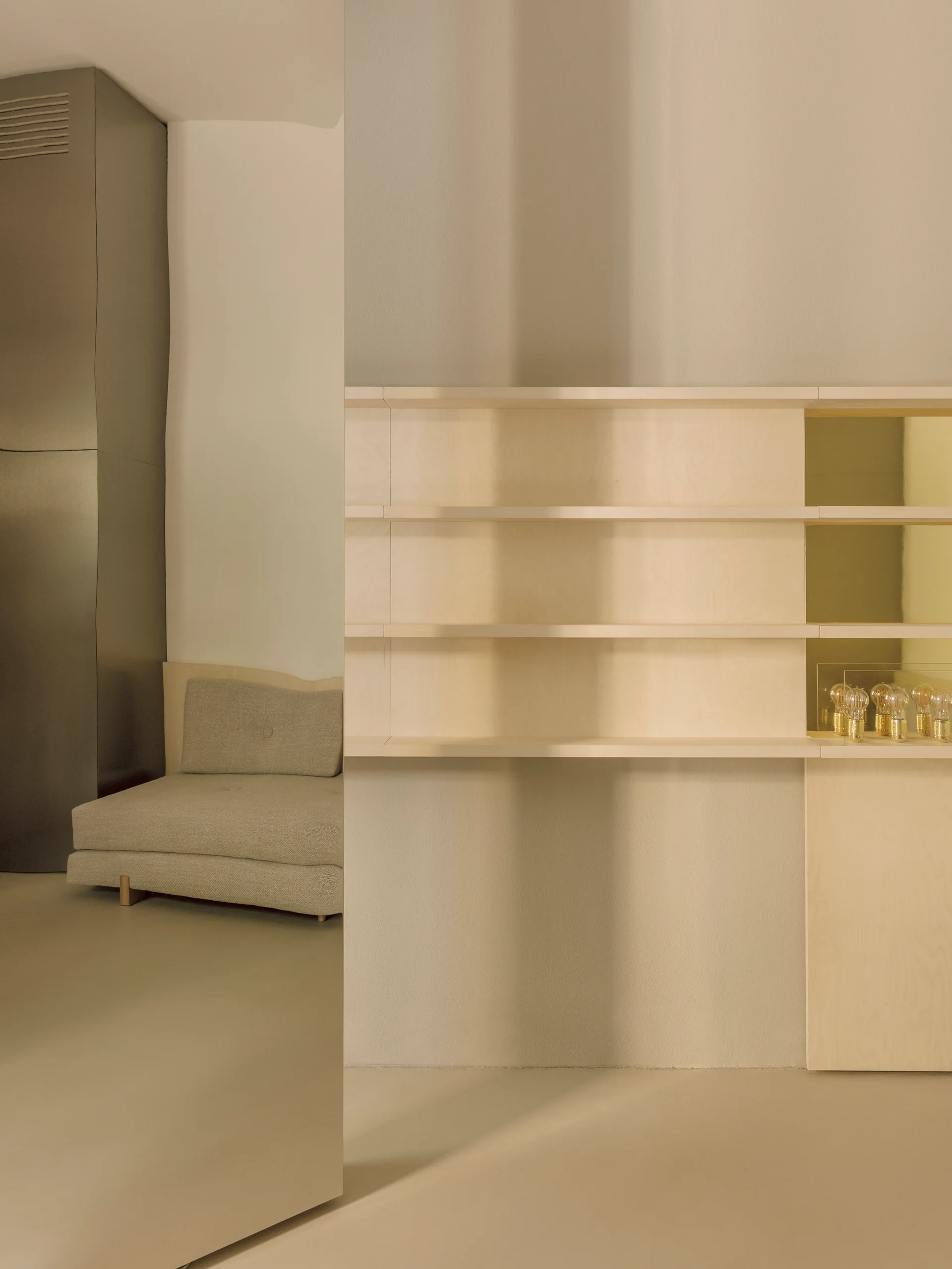 Minimalist beige interior featuring a light wood built-in shelving unit next to a gray upholstered sofa.