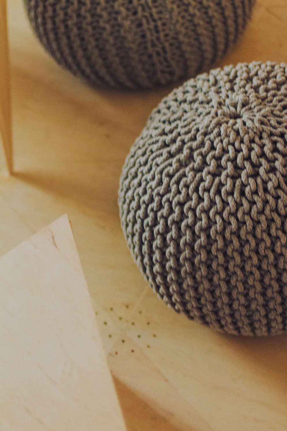 Two round, gray knitted pouf ottomans with a thick woven texture rest on a light-colored wood floor with visible grain.