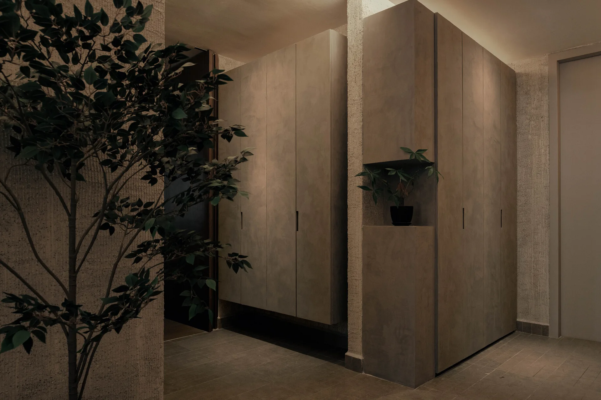 A minimalist grey hallway features built-in matte cabinets with an integrated lighted display niche and a textured plaster wall.