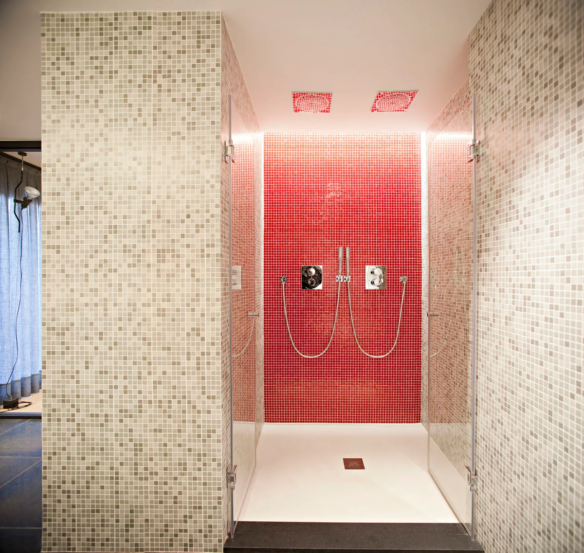A modern walk-in shower features a vibrant red mosaic tile back wall, grey mosaic tile side walls, and double metal shower fixtures.