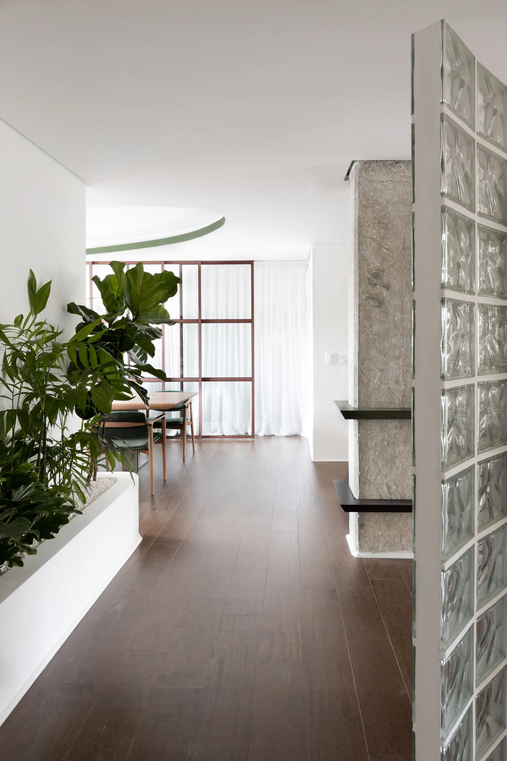 A modern transition space with dark wood flooring features a glass block partition, a raw concrete column, and a large built-in planter.