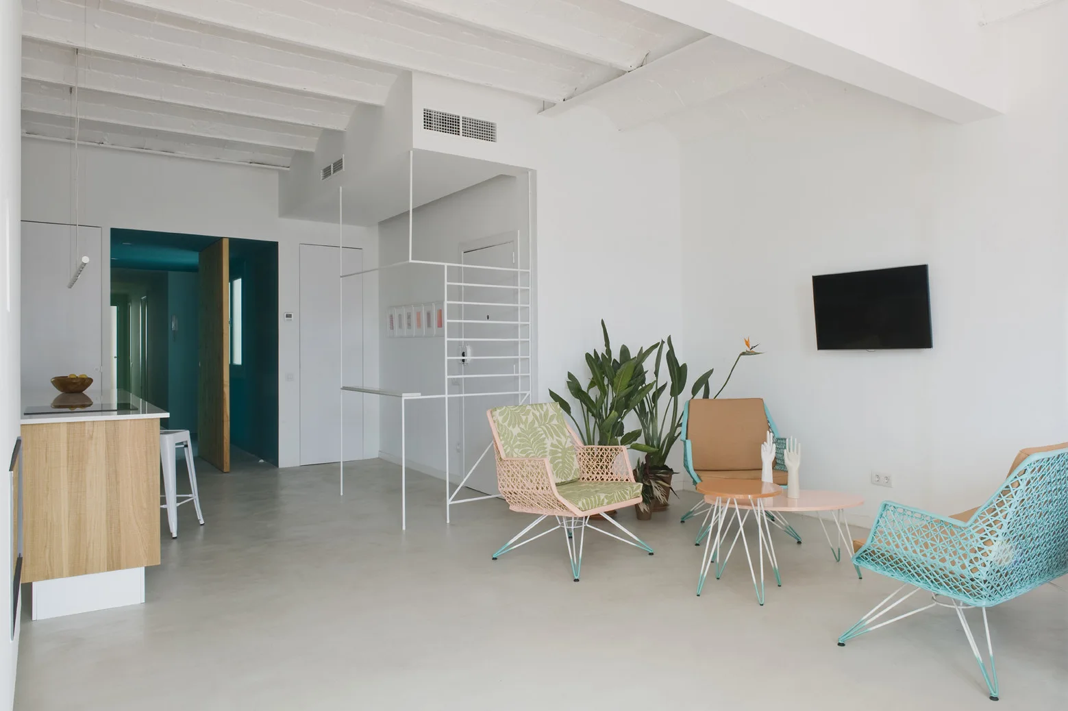 A bright living area features colorful woven armchairs, a pink coffee table, and an exposed white beam ceiling.