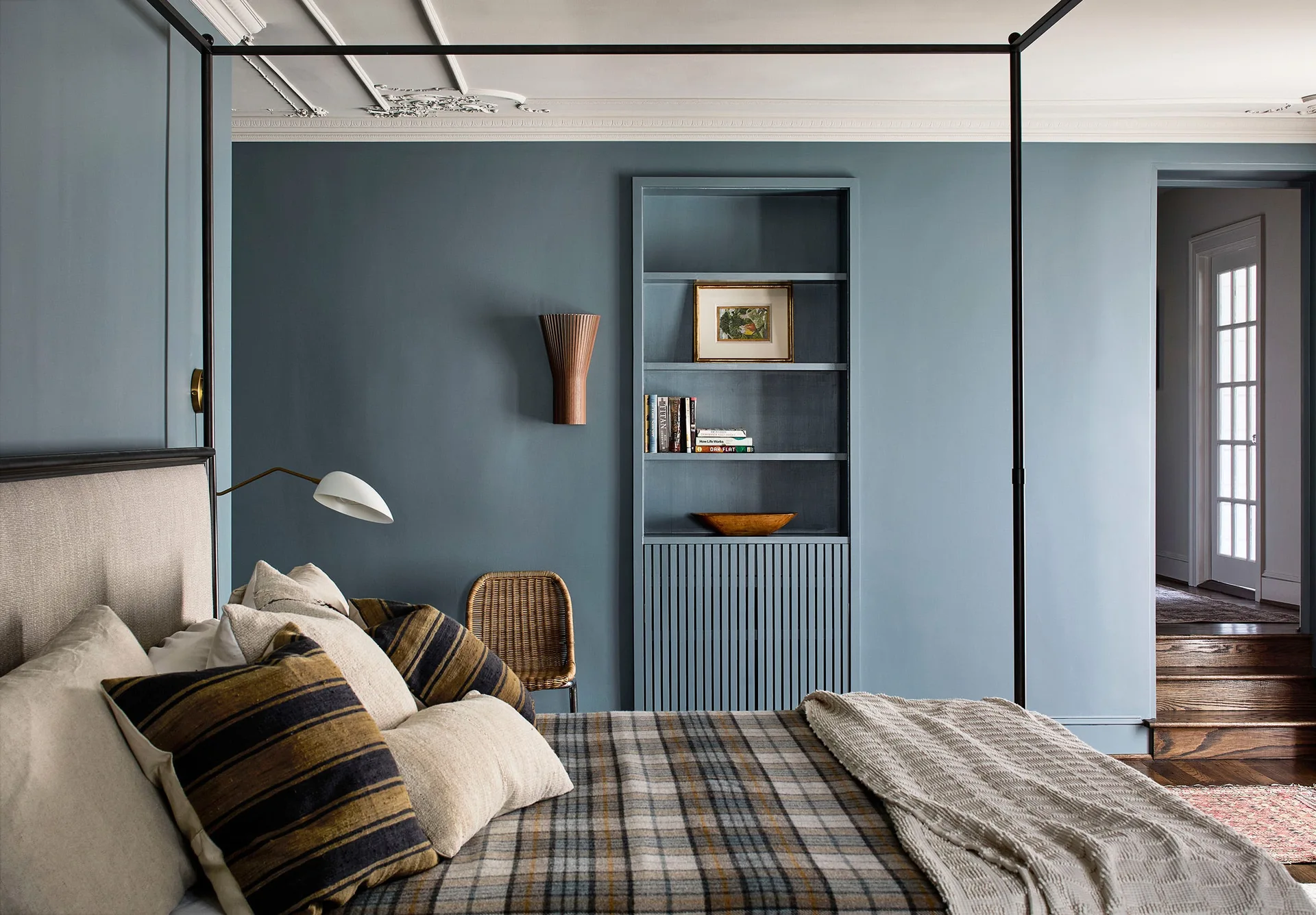 A transitional bedroom featuring dusty blue walls, an integrated matching bookshelf with fluted cabinet doors, and a black metal canopy bed.