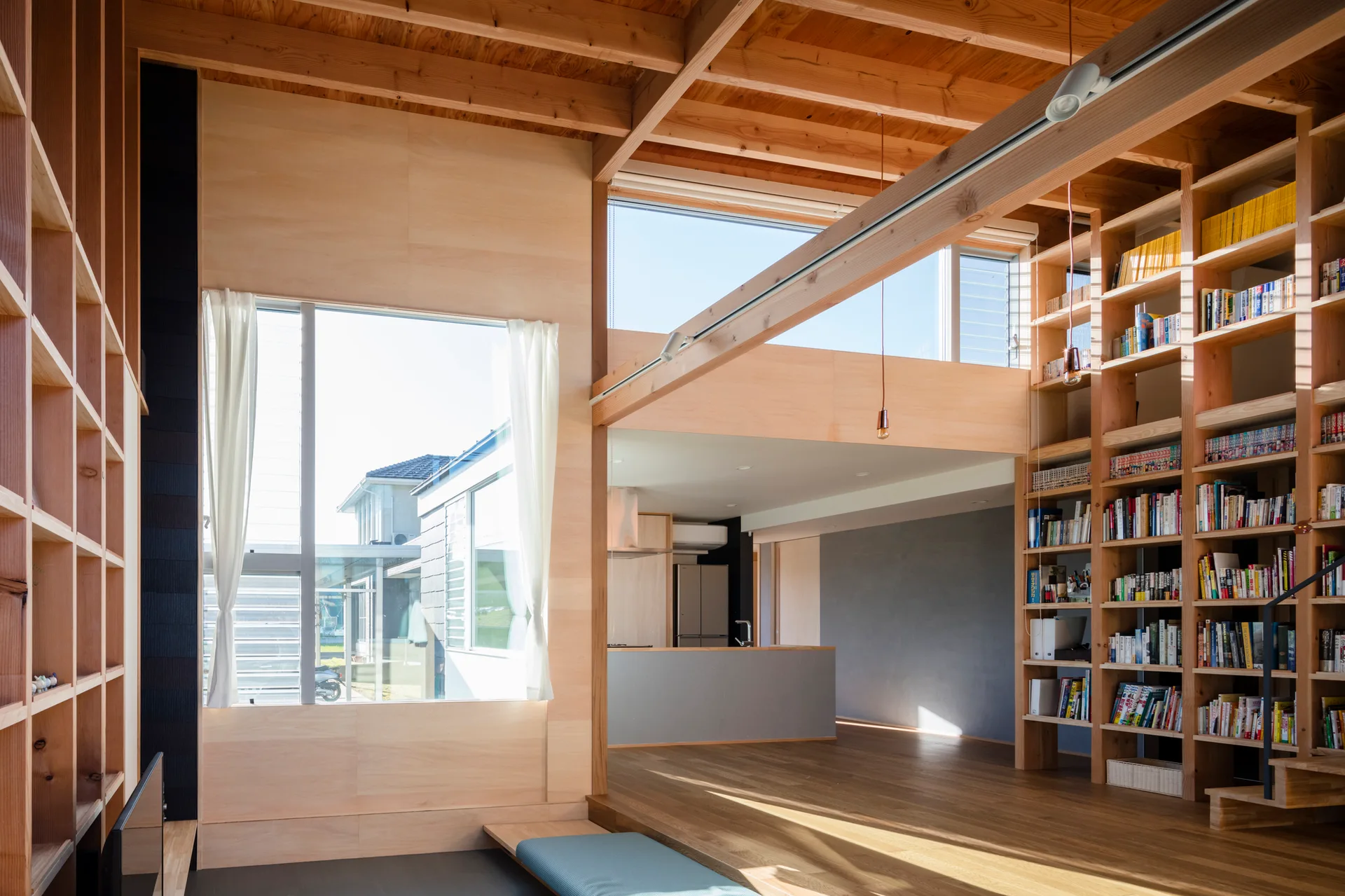 An open living space with light-colored plywood paneling, floor-to-ceiling wooden bookshelves, and exposed timber ceiling beams.