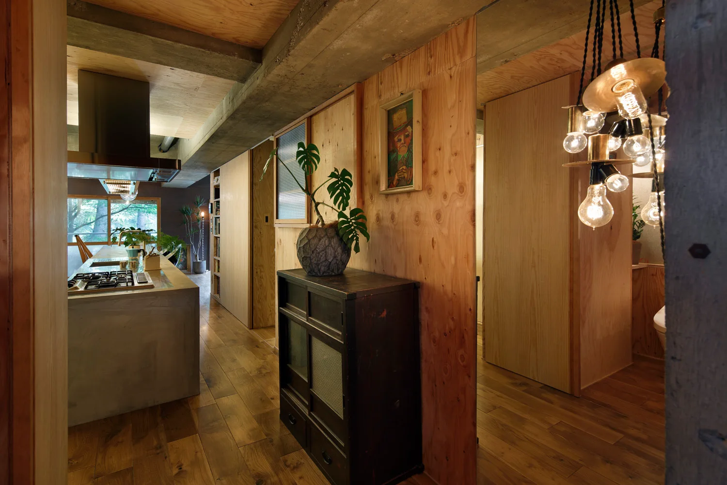 An industrial kitchen space features light plywood wall paneling, an exposed concrete ceiling beam, a concrete island, and a dark wood storage cabinet.