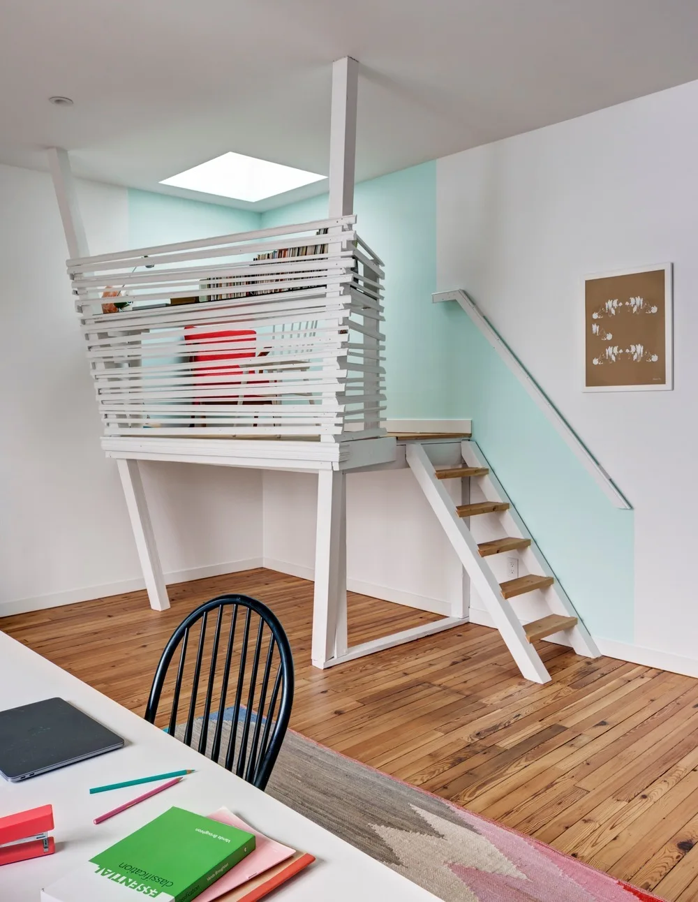 A bright home office features a raised white loft platform with wooden steps, a mint green accent wall, and a skylight above the desk.