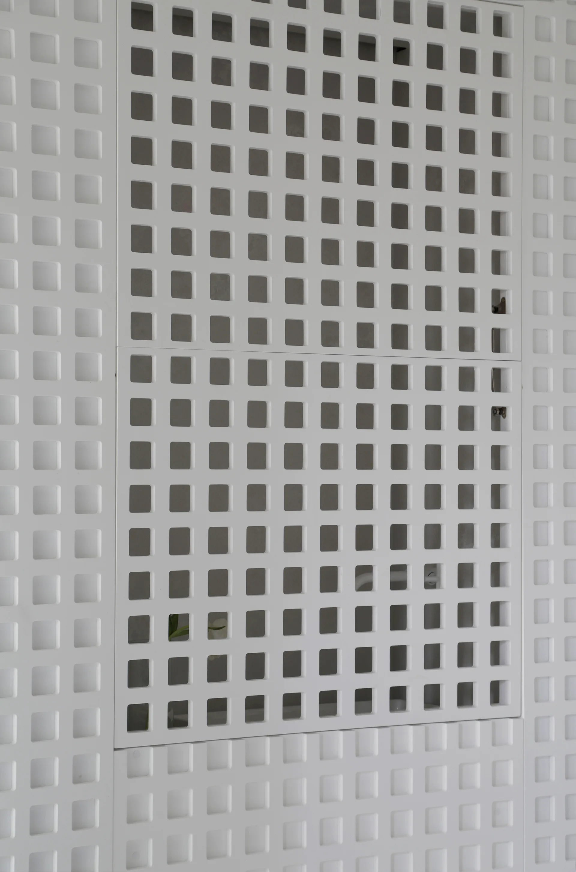 A close-up of a white interior wall covered in modular geometric panels with a repeating square grid cutout pattern.