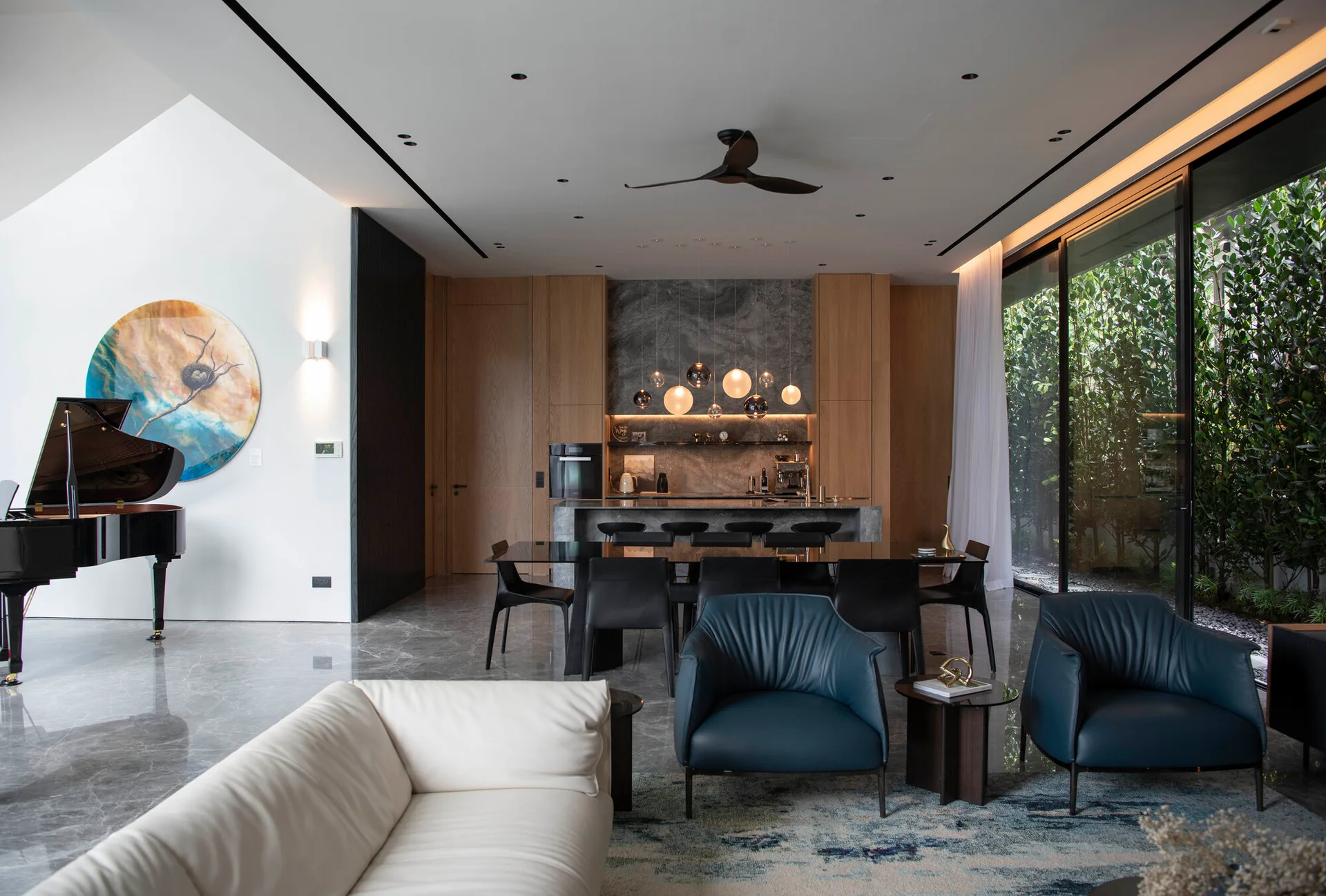 A spacious open-plan living room with white and navy seating features a grand piano, a dark dining table, and a kitchen with wood cabinetry.