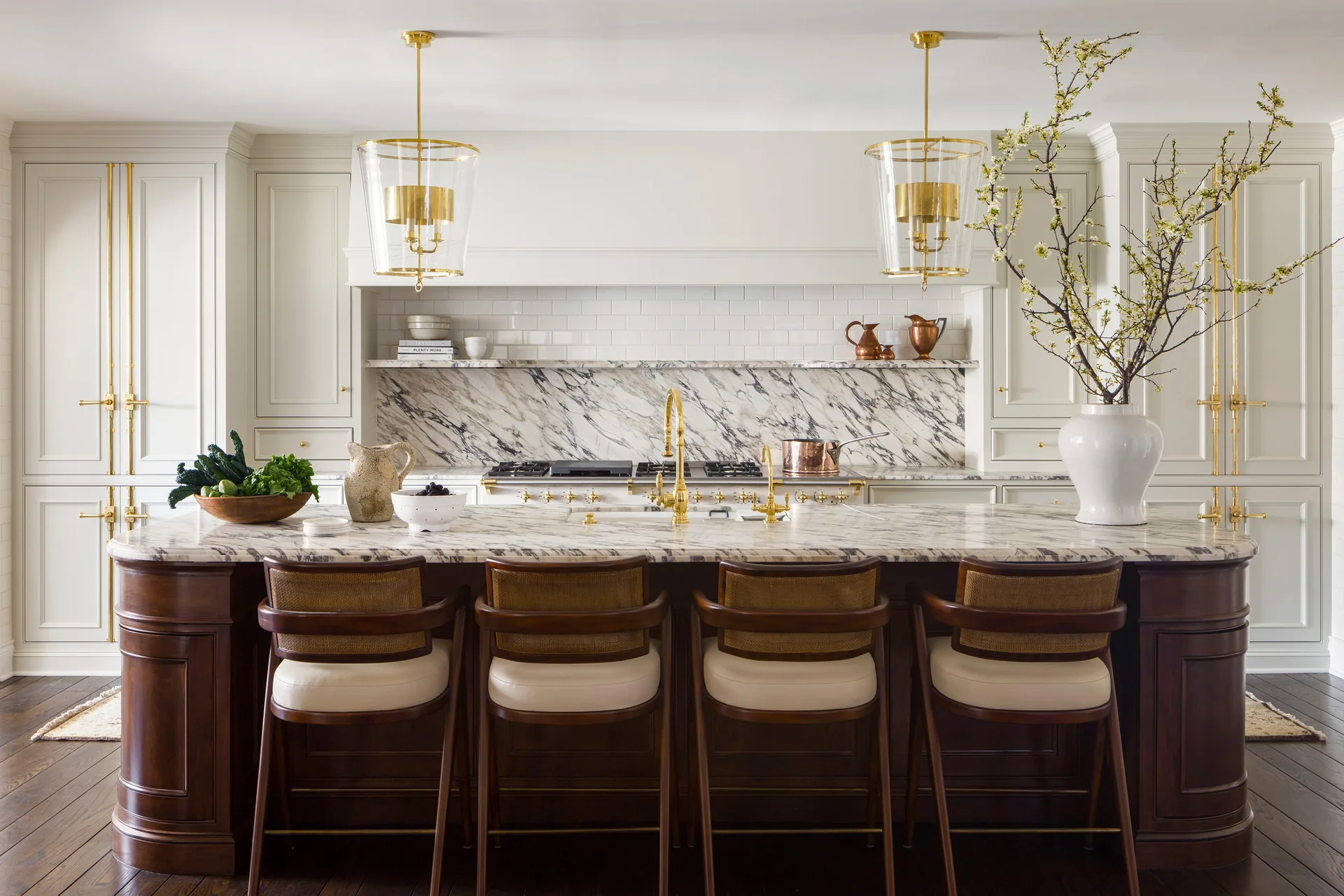 A dark wood kitchen island with veined marble countertops is surrounded by cane-backed bar stools and lit by two glass pendant lights.
