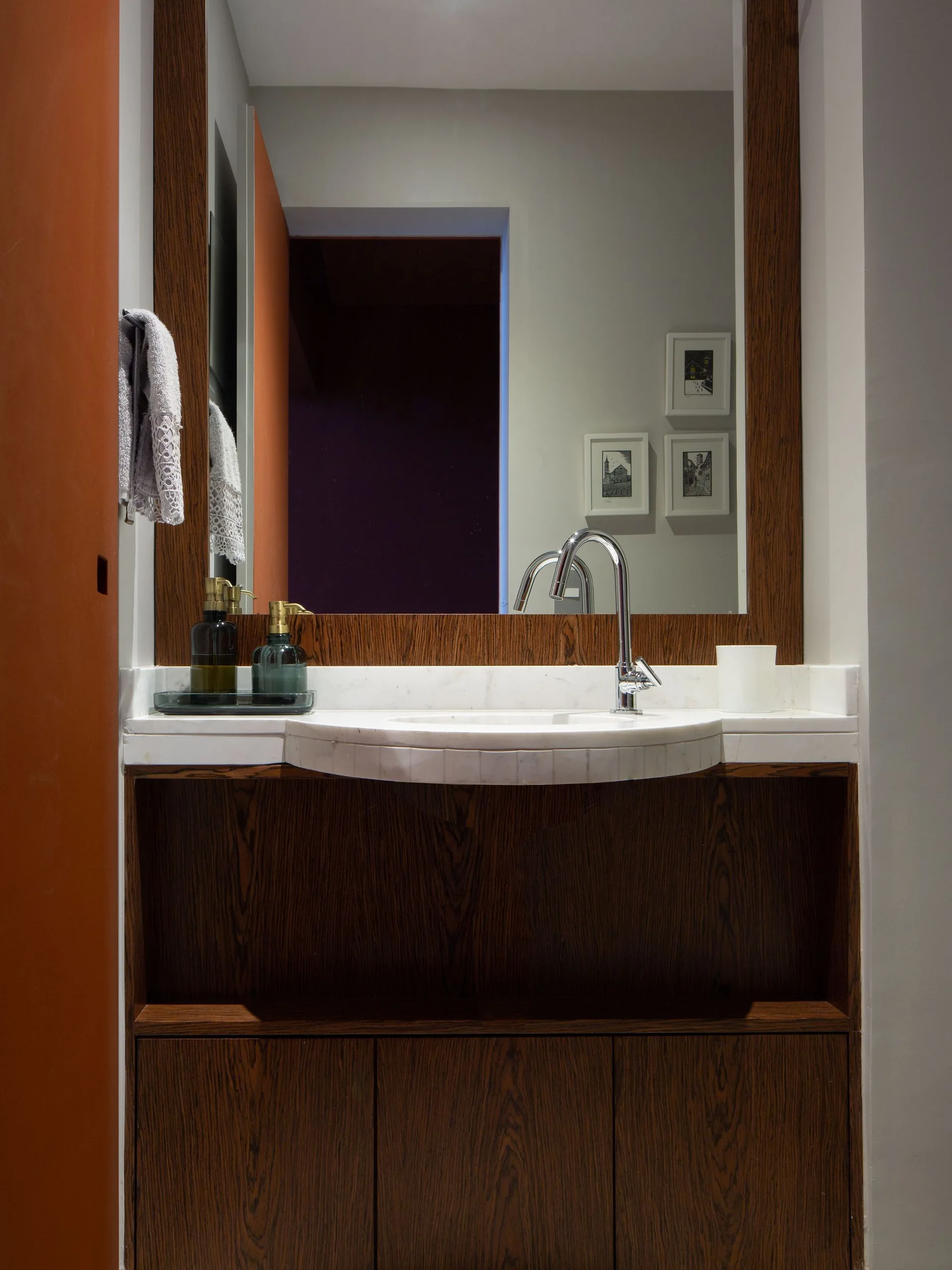 A modern bathroom vanity made of dark wood with a white marble countertop, a curved sink, a chrome faucet, and a large wood-framed mirror.