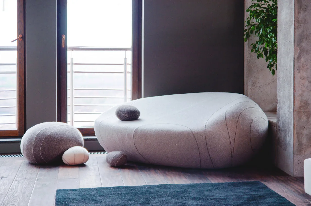 A contemporary living room featuring a large light grey pebble-shaped sofa, matching floor cushions, dark wood floors, and a concrete column.
