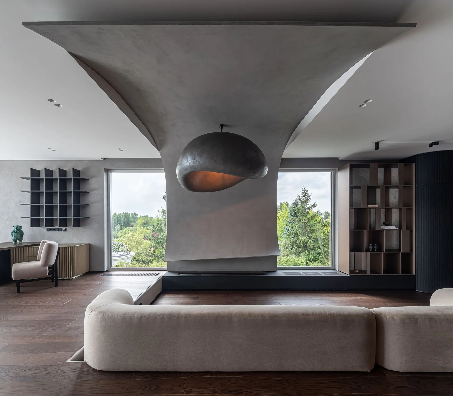 A minimalist living room with a curved concrete fireplace column, a large dome pendant light, a beige sofa, and wood floors.