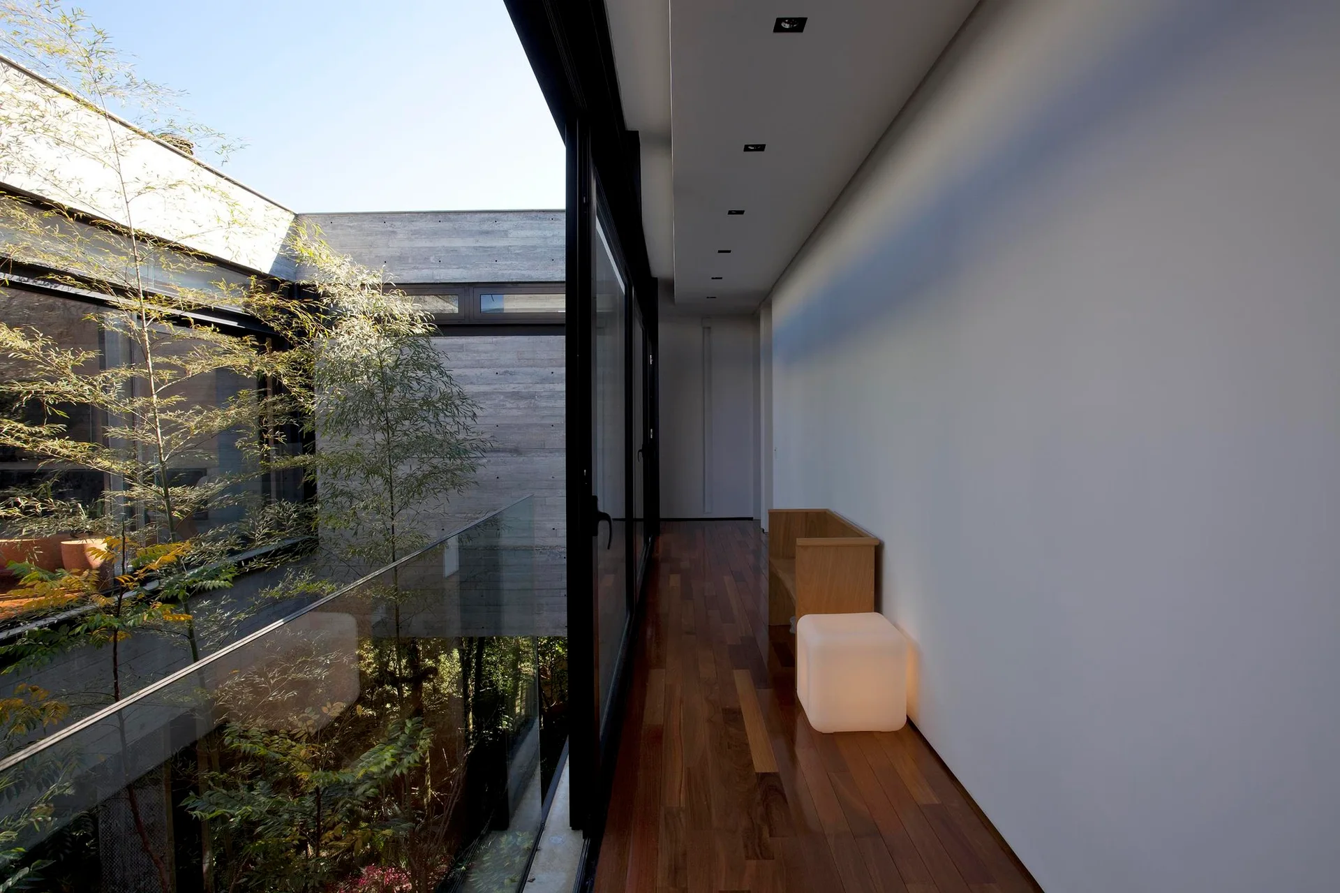 A minimalist hallway with wood plank flooring features large sliding glass doors looking out onto a central green courtyard with bamboo trees.